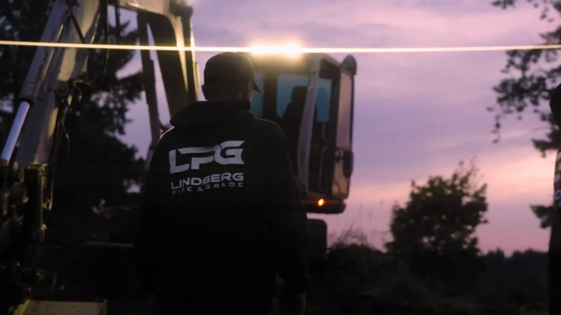 LPG crew member in a company hoodie walking out to an excavator at dusk