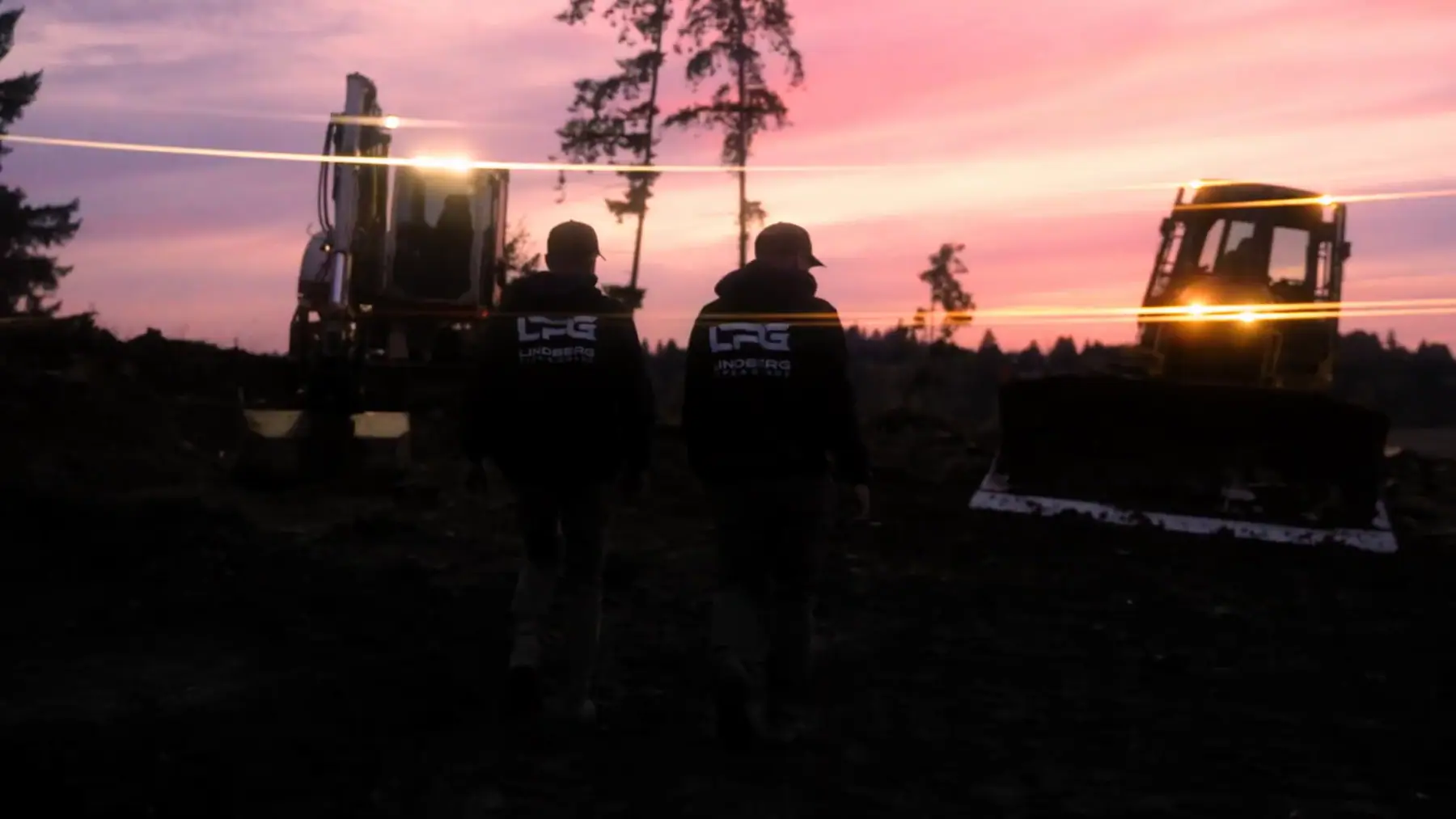 Two LPG crew members in company hoodies walking out to the excavator and dozer at sunrise