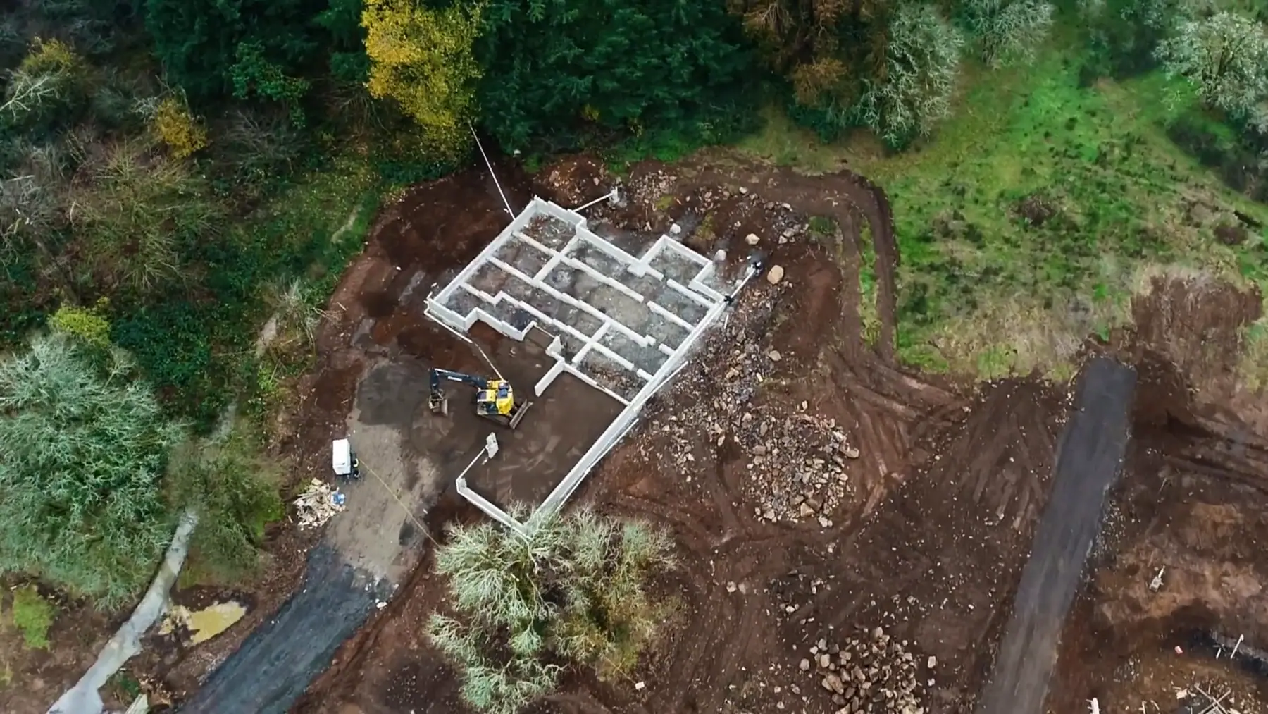 Aerial view of a custom home foundation cut into a wooded hillside lot