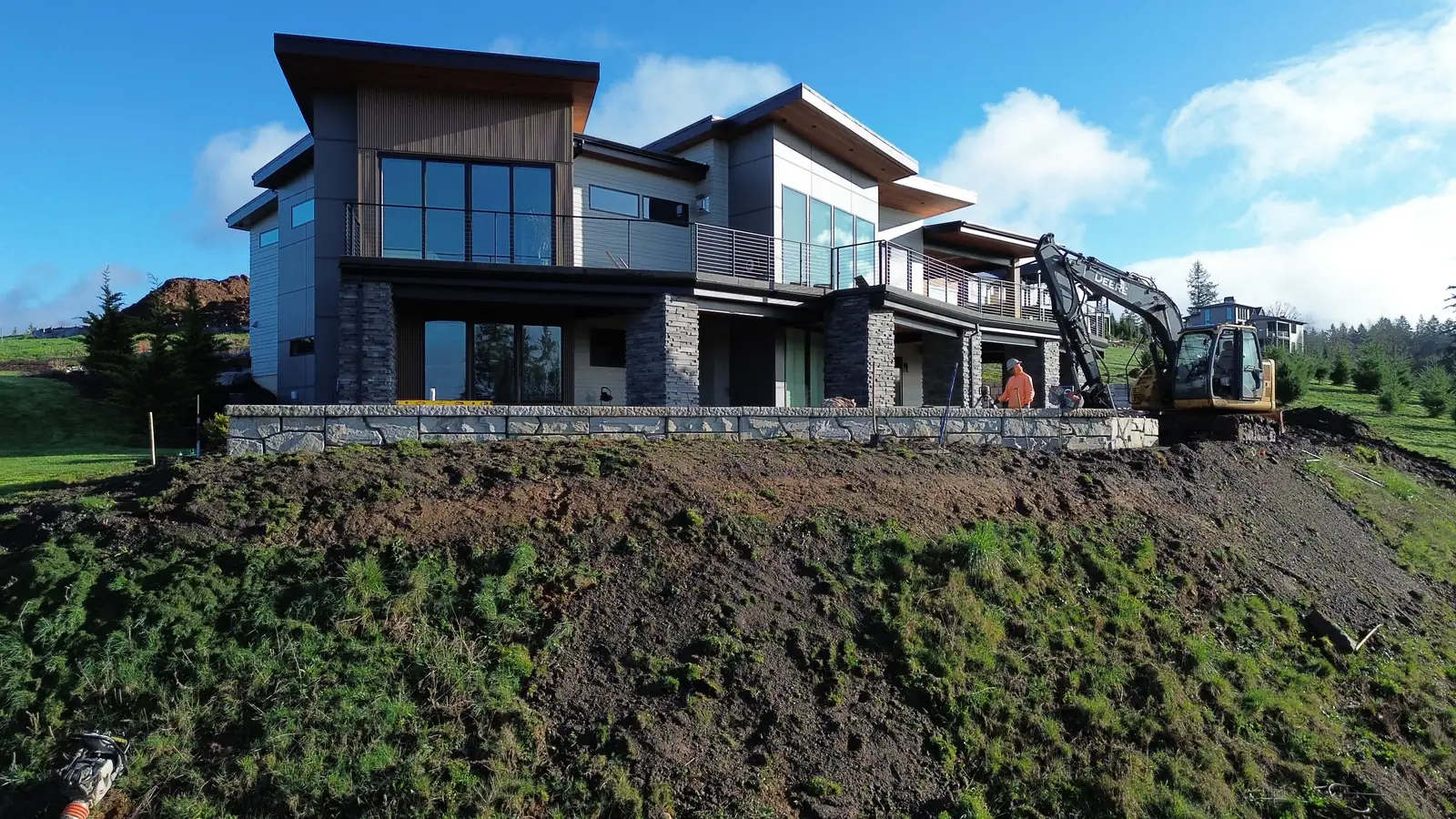 Finished grade and stone wall below a custom hillside home, with LPG's excavator on site