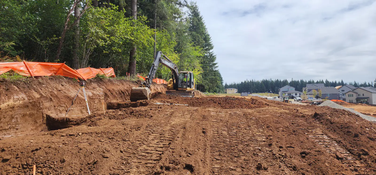 LPG excavator digging a building pad beside a new subdivision